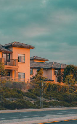 A modern, two-story orange house with a tiled roof, surrounded by greenery under a cloudy sky.